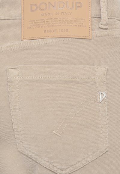 Pantaloni di velluto a coste beige con tasca posteriore, etichetta di marca in pelle DONDUP e spilla metallica con logo "D" sul bordo della tasca.