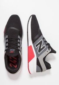 Černé atletické tenisky s prodyšným síťovaným svrškem, šedými akcenty, červenými detaily a bílou podrážkou. Design obsahuje výrazné logo "N".