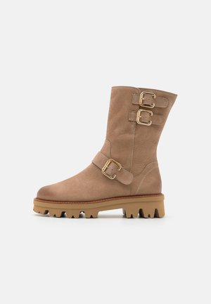 Bottine en cuir beige à talon, avec deux sangles à boucle, un bout arrondi et une semelle en caoutchouc robuste dotée d'un motif de traction prononcé.