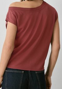 Haut bordeaux à manches courtes avec un design dégarni, texture lisse, col côtelé et coupe décontractée, associé à un jean en denim foncé.