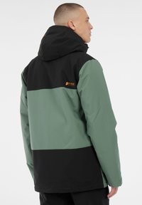 Giacca impermeabile con un design a blocchi di colore nero e verde, dotata di cappuccio e logo sul retro, realizzata in tessuto morbido.