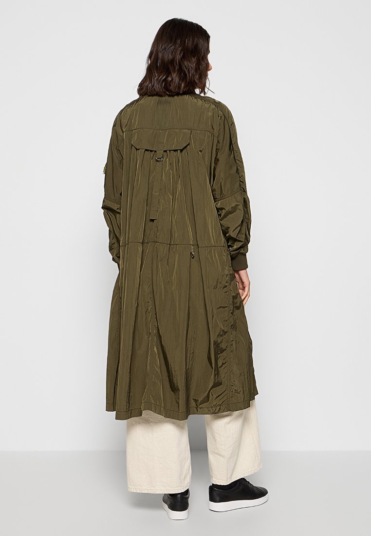 Zielono-oliwkowy, lekki długi płaszcz z marszczonym tyłem, elastycznymi mankietami i dwoma bocznymi kieszeniami. Gładki, teksturowany materiał o luźnym fasonie.