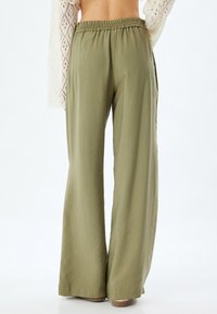 Pantalons larges kaki en tissu léger, dotés d'une taille élastique et d'une texture lisse, avec une coupe décontractée jusqu'aux chevilles.