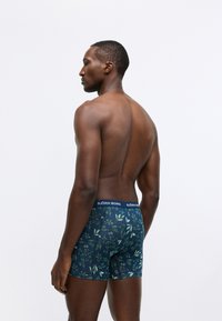 Tamsiai mėlynos boxer tipo apatinės kelnės su žaliai lapų raštu. Minkšta medžiaga su tvirtu prigludimu, turi firminę elastinę juostą.