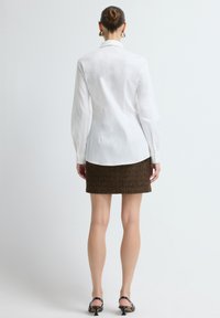 Witte blouse met lange mouwen en een achterpand, gecombineerd met een bruine gestructureerde rok. Soepele stof, getailleerde pasvorm, rechte zoom en simpele kraag.