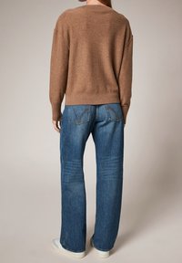 Bruine trui met een ontspannen pasvorm, geribde manchetten en onderrand, gecombineerd met blauwe denim jeans met een rechte snit en gestikte achterzakken.