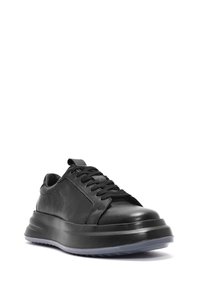 Sneaker in pelle nera con punta arrotondata, superficie testurizzata, lacci piatti e suola spessa e rialzata. Il design presenta una finitura liscia e accenti sottili.