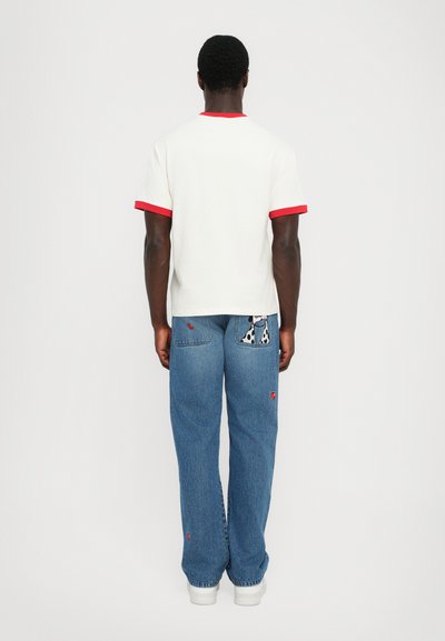 Hvid T-shirt med rød krave og ærmeakcenter, parret med lyseblå denimjeans med broderede detaljer og lommer.
