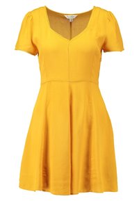 Gul kortärmad klänning med V-ringning och figursydd överdel, utsvängd kjol och mjuk textur. Inga synliga mönster eller detaljer.