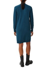 Abito in maglia color teal, maniche lunghe, polsini e orlo a coste. Abbinato a stivaletti neri in pelle alla caviglia. Tessuto morbido, vestibilità leggermente ampia.