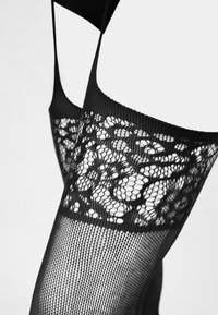 Czarne pończochy z siateczki z dekoracyjnym wzorem koronki na górnej opasce, charakteryzujące się gładką fakturą i dopasowanym krojem.