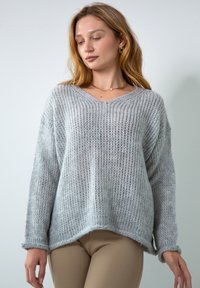 Jasnoszary sweter dzianinowy z dekoltem w serek, obniżonymi ramionami i prążkowaną strukturą. Posiada luźny krój oraz lekko wydłużony tylny brzeg.
