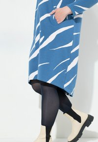 Blauwe jurk met witte abstracte strepen, met een zak. Gecombineerd met zwarte leggings en crèmekleurige enkellaarsjes met zwarte accenten.
