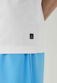 White textured athletic shirt with a black logo on the side, paired with light blue shorts featuring a ribbed pattern.