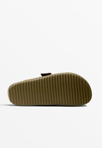 Sandal med en flexibel beige gummisula som har horisontella rännor och ett brunt textilband för säker passform.