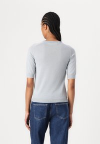 Pulover tricotat cu mâneci scurte, de culoare gri deschis, cu un guler și manșete cu nervuri, asortat cu blugi de denim de culoare albastru închis, cu buzunare la spate.