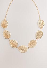 Gold necklace featuring a series of leaf-shaped links with intricate cut-out patterns, connected by a fine chain.