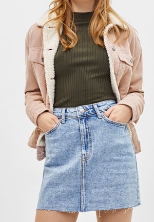 Fløjlsjakke i blød lyserød med falsk lammeskindskrave, ribstrikket mørkegrøn top og lyseblå denimnederdel med frynset kant og forlommer.