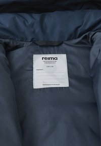 Interno in tessuto impermeabile di colore blu navy, con un'etichetta che mostra il marchio "Reima", la taglia "128 / 8Y" e le istruzioni per la cura.