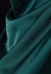 Tissu satin teal parsemé de petits strass verts et transparents, montrant des plis doux et une texture lisse et brillante.