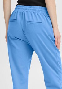 Light blue sweatpants with an elastic waistband, smooth texture, and two back pockets. Simple design, suitable for casual wear.