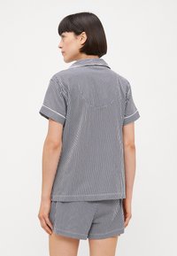 Kortärmad pyjamasett i marinblå och vita vertikala ränder. Cottontyg, knäppning framtill med krage, matchande shorts med rullade fållar.