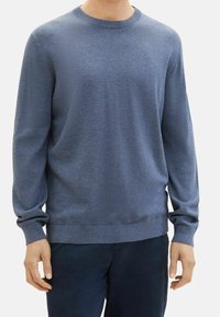 Pull en maille bleu à manches longues, col rond et poignets côtelés. Texture lisse avec une subtile variation tonale et un logo sur la poitrine.