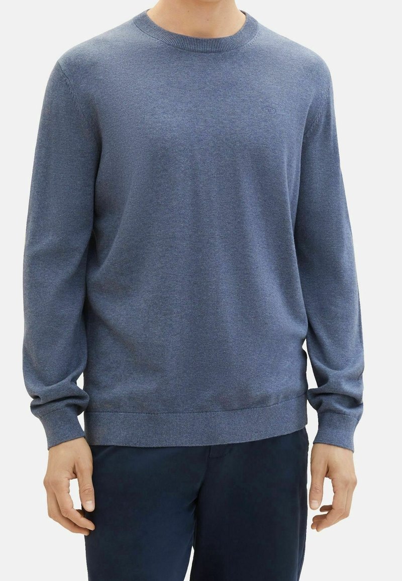 Pull en maille bleu à manches longues, col rond et poignets côtelés. Texture lisse avec une subtile variation tonale et un logo sur la poitrine.