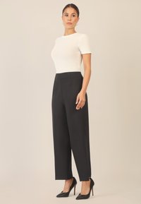 Haut blanc ajusté à manches courtes associé à un pantalon noir taille haute et des escarpins noirs à bout pointu. Tissu lisse avec un design ajusté.