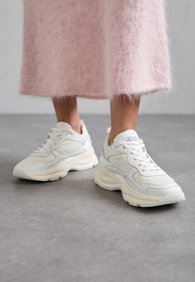 Baskets blanches en matériaux mesh et cuir, à bout arrondi et semelle rembourrée. Elles disposent de lacets et du nom de la marque sur la languette.