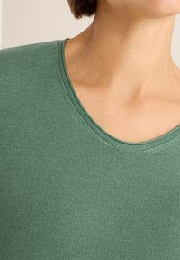 Grüner kurzärmeliger Oberteil aus geripptem Stoff, mit weitem Ausschnitt und glatter Textur. Details umfassen eine figurbetonte Silhouette.