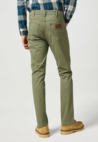 Pantalones de algodón verde oliva con un corte ajustado, bolsillos traseros con costuras en zigzag y una etiqueta de cuero en la cinturilla.