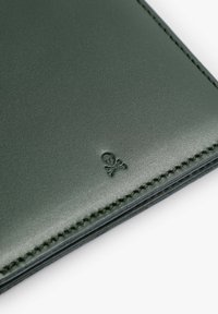 Portofel verde din piele cu o textură netedă, având detalii brodate cu craniu și oase încrucișate, și cusături contrastante pe margine.