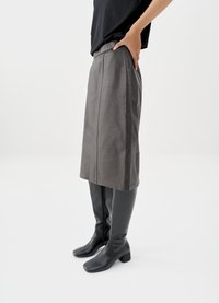 Pilko odos sijonas tiesia kirpimu, derinamas su juodais kelių aukščio batais su blokuota kulne ir lygiu paviršiumi. Paprastas dizainas.