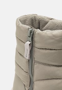 Beige isolierte Stiefel mit gepolsterten Einsätzen und strukturiertem Innenfutter. Mit einem zentralen Reißverschluss und Zugschlaufe sowie genähten Akzenten.