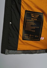 Vnútro čiernej a oranžovej bundy s produktovým označením PME Legend Dee-Icer spolu so špecifikáciami a ikonami materiálu.