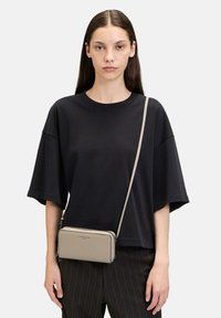 Beżowa skórzana torba na ramię o fakturowanym wykończeniu, srebrne zamki błyskawiczne i smukły design. Wyposażona w długi, regulowany pasek.