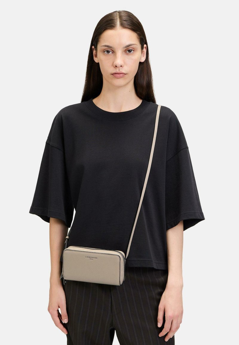 Beige lederne Umhängetasche mit strukturiertem Finish, silbernen Reißverschlüssen und schlankem Design. Verfügt über einen langen, verstellbaren Tragegurt.