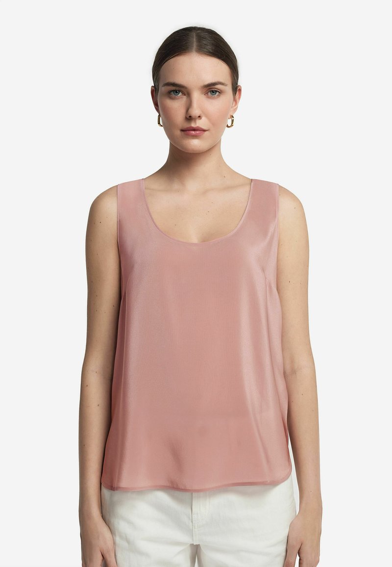 Ärmlös topp i ljusrosa genomskinlig tyg, med en bred rund halsringning och flödande siluett, matchad med vita högmidjade byxor.