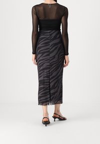 Haut noir à manches longues associé à une jupe mi-longue à motifs zèbres noirs et gris, avec un ourlet festonné et une coupe slim. Sandales à talons noires.