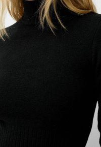 Suéter negro de punto con un cuello alto, textura acanalada en el dobladillo y en los puños, y una apariencia de tela suave.