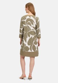 Grön och vit knälång klänning med ett bladmönster, trekvartsärmar och en enfärgad khakifärgad fåll. Släta tyget med en avslappnad passform.