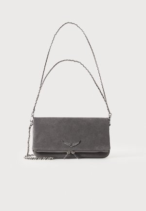 Sac à bandoulière en daim gris foncé avec rabat, bandoulière à chaîne argentée et petit emblème en forme d’aile sur fond uni.