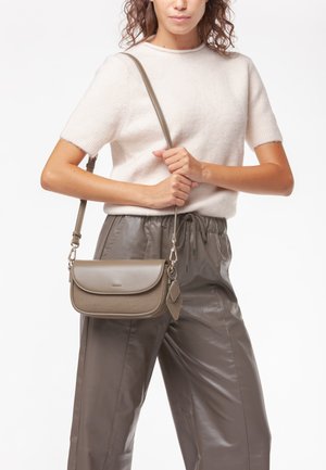 Borsa a tracolla grigia con design strutturato, dotata di chiusura a patta e pannello testurizzato. Modello che indossa un maglione leggero e pantaloni a sigaretta.