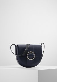 Borsa a tracolla in pelle blu navy con un accent metallici circolare, patta superiore piatta e una tracolla nera a contrasto. Base rotonda, texture liscia.