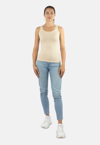Beige ärmelloses Tanktop kombiniert mit hellblauen Skinny Jeans und weißen Sneakern. Glattes Gewebe mit tailliertem Design, lässiger Stil.