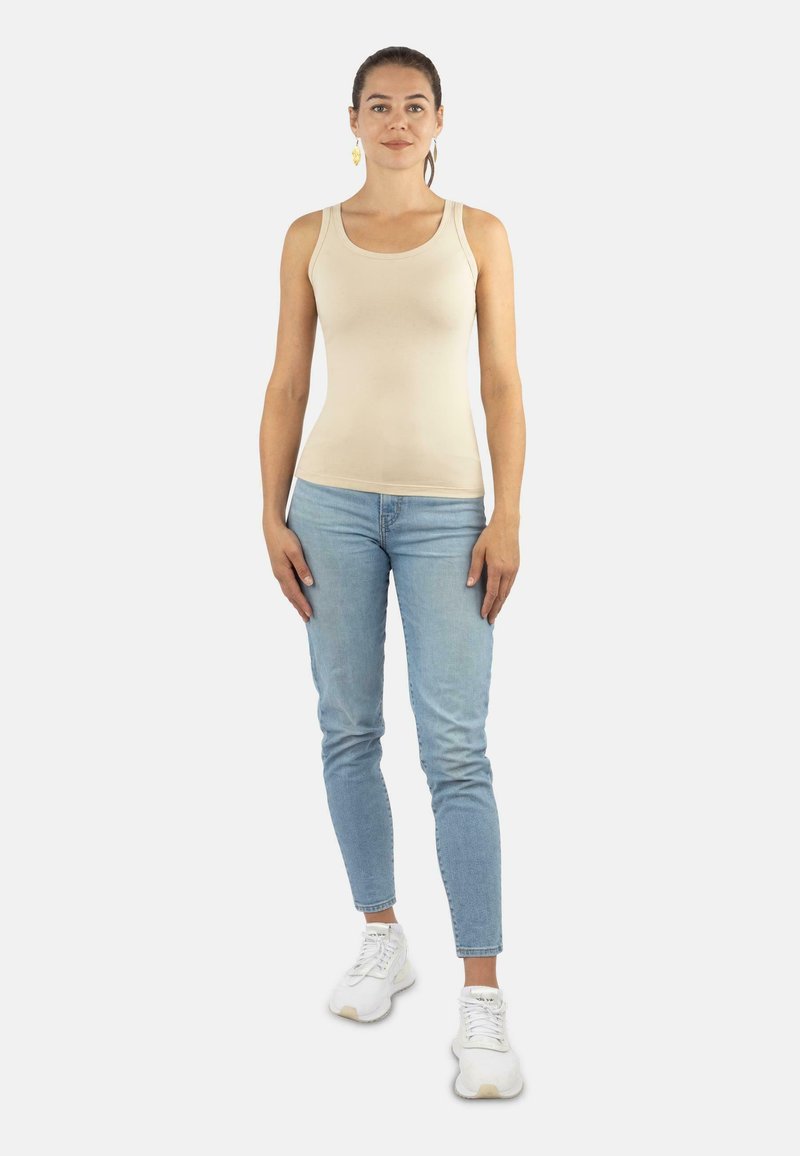 Beige ärmelloses Tanktop kombiniert mit hellblauen Skinny Jeans und weißen Sneakern. Glattes Gewebe mit tailliertem Design, lässiger Stil.
