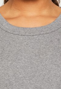 Szara dzianina prążkowana z okrągłym dekoltem. Tekstura jest gładka z delikatnym wzorem, podkreślającym swobodny charakter ubrania.