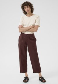 Beige t-shirt met korte mouwen gecombineerd met bordeauxrode wijde broek met voorzakken en een knoopsluiting, aangevuld met zwarte sandalen.