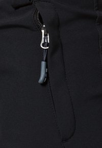 Detailný záber na zips čiernej bundy so šedou gumovou ťahacou šnúrou pripevnenou na textilnom očku.
